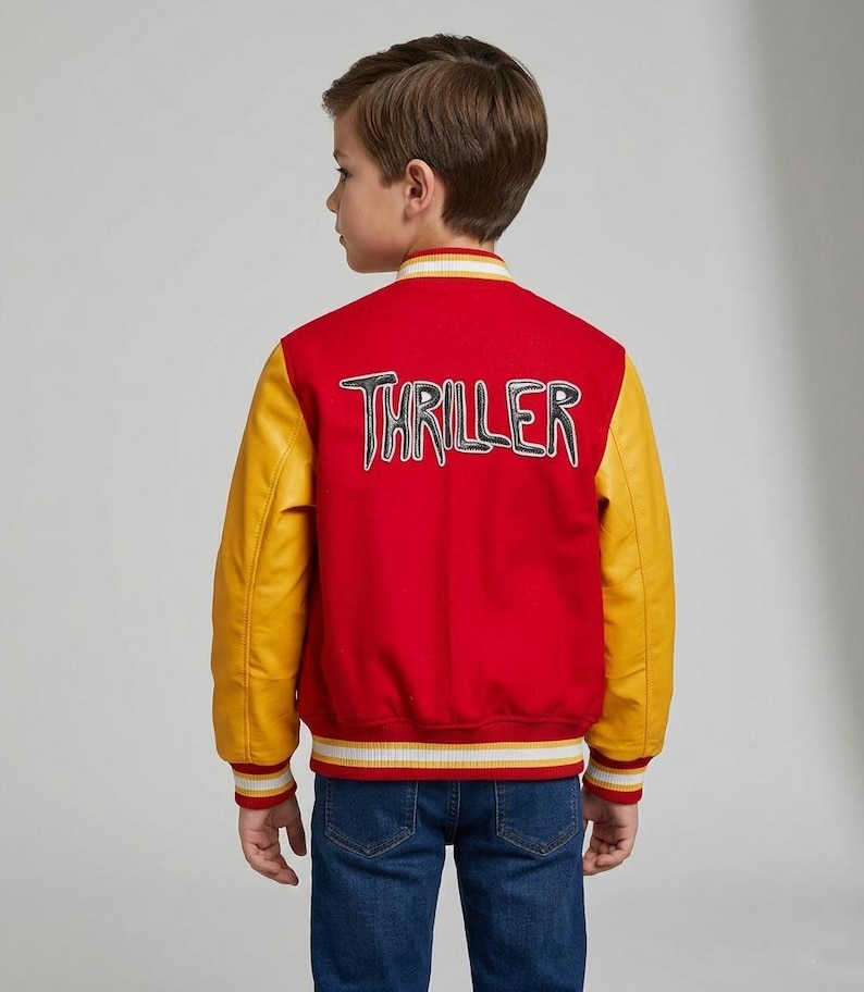 May include: A red varsity jacket with yellow sleeves and striped ribbed trim at the collar, cuffs, and hem. The back features the word THRILLER in large, stylized white and black lettering. The jacket is worn over blue denim jeans.