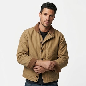 May include: A tan canvas jacket featuring a brown corduroy collar and matching corduroy cuffs. The jacket has a button-front closure with visible dark buttons and long sleeves. It is worn over a plain black shirt and blue denim jeans.