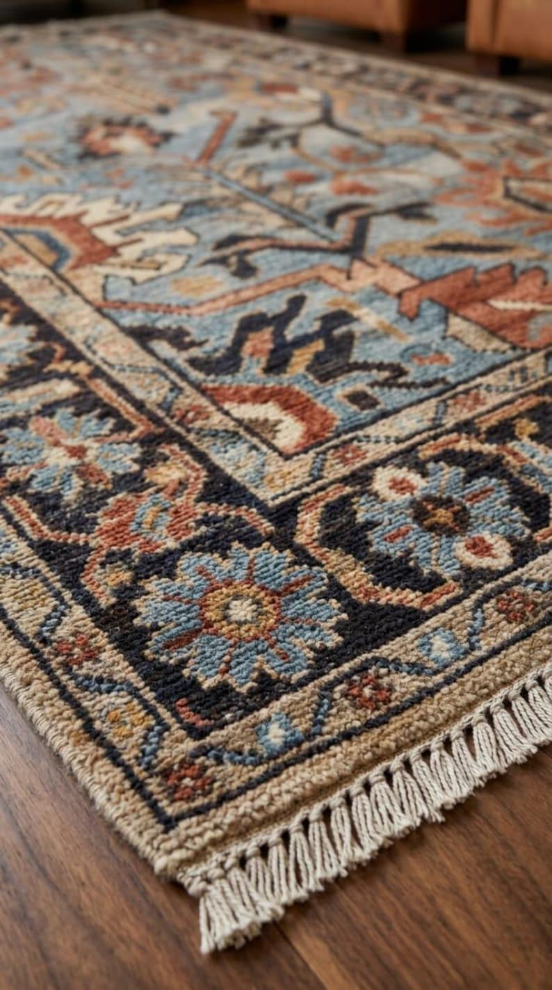 May include: A rectangular area rug featuring a complex pattern of floral and geometric motifs in shades of light blue, rust orange, dark navy, and beige. The rug has a thick, textured pile and is finished with short, off-white fringe at the ends.