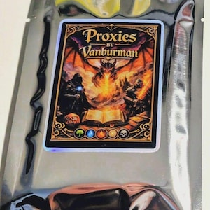 May include: A trading card pack with a card displaying the text "Proxies by Vanburman." The card art shows a dragon breathing fire, flanked by figures. The pack is sealed in a silver foil pouch.