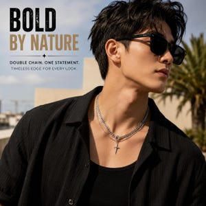 Op de afbeelding: Een zilveren dubbele ketting met een centrale stervormige hanger. Het sieraad wordt gedragen met een zwart overhemd en een zwarte zonnebril. De tekst op de afbeelding luidt: BOLD BY NATURE, DOUBLE CHAIN. ONE STATEMENT. TIMELESS EDGE FOR EVERY LOOK.