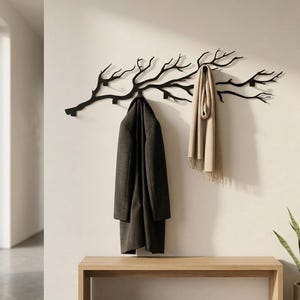 May include: A black metal coat rack in the shape of a tree branch, with a dark grey coat and a beige scarf hanging from it. A light wood bench is below, with black shoes. A potted plant is on the right.