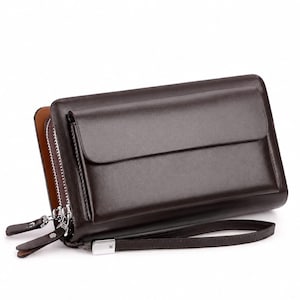 Op de afbeelding: Een donkerbruine leren clutch met een rechthoekige vorm, voorzien van een voorvak met klep, twee hoofdvakken met rits en zilverkleurige metalen hardware, inclusief een afneembare polsband bevestigd aan een zilveren metalen connector aan de zijkant.