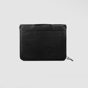 Op de afbeelding: Een rechthoekige zwarte leren laptoptas met een handvat aan de bovenkant en een zilverkleurige metalen ritssluiting aan de zijkant. De tas heeft een gladde, consistente textuur op het voorpaneel en een strak, gestructureerd ontwerp.