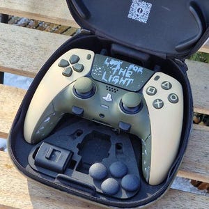 May include: Open black carrying case with a custom video game controller. The controller is olive green and beige with the text "Look for the Light". The case also contains a stop sign sticker and other accessories.