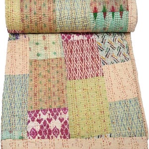 Peut inclure: Une courtepointe patchwork avec un bord supérieur enroulé. La courtepointe présente une variété de couleurs et de motifs, notamment des carrés vert clair, roses et bleus. La courtepointe est faite de tissu cousu.