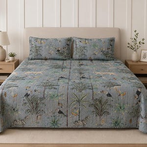 Op de afbeelding: Blauwe quiltset met een junglepatroon met zebra's, toekans en palmbomen. De set bevat een quilt en twee bijpassende kussenslopen. Het beddengoed is gemaakt van een zachte, gewatteerde stof.