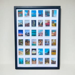 Puede incluir: Una obra de arte enmarcada en negro que presenta una cuadrícula de pequeñas fotografías. Las fotografías representan varios paisajes y escenas, incluyendo edificios, naturaleza y cuerpos de agua. El marco es rectangular y tiene un paspartú blanco.
