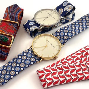 Könnte beinhalten: Uhren mit gemusterten Armbändern und goldfarbenen Gehäusen. Eine Uhr hat ein blaues Paisley-Armband, eine andere ein blaues Armband mit einem kreisförmigen Muster und eine dritte ein rotes Armband mit einem weißen Vogelmuster. Ein rotes Paisley-Armband mit goldener Schnalle ist ebenfalls abgebildet.