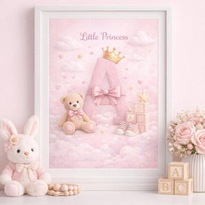 Puede incluir: Un estampado rosa enmarcado para guardería con las palabras "Little Princess" sobre una gran letra "A" adornada con una corona dorada y un lazo. También se incluyen un osito de peluche, zapatos de bebé y bloques que deletrean "A B". Un conejito de peluche y flores están en el estante.