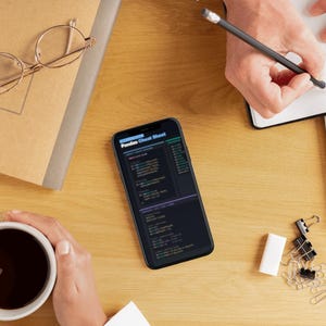 Puede incluir: Vista superior de un escritorio de madera con un smartphone que muestra una "Pandas Cheat Sheet". Otros elementos incluyen una taza de caf&eacute;, un cuaderno, gafas y material de oficina. Una persona escribe en un cuaderno con un l&aacute;piz.