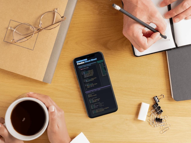 Puede incluir: Vista superior de un escritorio de madera con un smartphone que muestra una "Pandas Cheat Sheet". Otros elementos incluyen una taza de caf&eacute;, un cuaderno, gafas y material de oficina. Una persona escribe en un cuaderno con un l&aacute;piz.