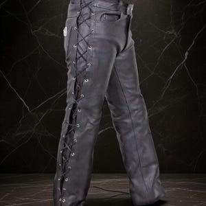 Könnte beinhalten: Schwarze Lederhose mit Schnürdetails an den Seiten. Die Hose hat ein klassisches Fünf-Taschen-Design und einen Knopfverschluss. Das Leder scheint leicht abgenutzt zu sein, was ihm einen robusten Look verleiht.