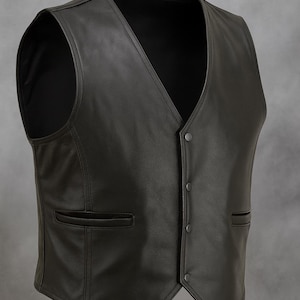 Könnte beinhalten: Eine schwarze Lederweste mit V-Ausschnitt und Knopfverschluss. Die Weste hat zwei Vordertaschen und eine taillierte Passform. Ein klassischer Stil, geeignet für verschiedene Anlässe.