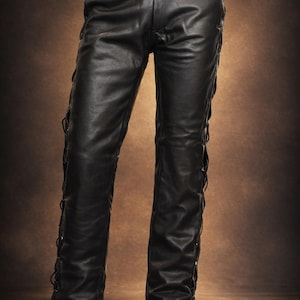 Könnte beinhalten: Schwarze Lederhose mit klassischem Fünf-Taschen-Design und Gürtel. Die Hose hat dekorative Schnürdetails entlang der äußeren Nähte. Die Lederhose wird vor einem braunen Hintergrund gezeigt.