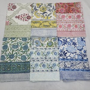 May include: A collection of folded fabric textiles with various floral and geometric patterns. The textiles feature a range of colors, including blue, pink, yellow, and green, with striped and patterned borders. The fabrics are likely cotton or linen.