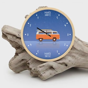 Puede incluir: Un reloj de pared redondo con marco de madera clara. La esfera del reloj presenta un fondo azul con una furgoneta naranja y blanca que transporta tablas de surf. Las palabras "MARÉE HAUTE" y "MARÉE BASSE" están impresas.