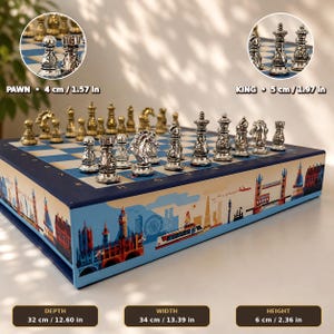 May include: A chess set with silver and gold-toned metal pieces on a blue and white board. The board features a London cityscape illustration. Dimensions are 12.60 inches deep, 13.39 inches wide, and 2.36 inches high. Pawns are 1.57 inches and kings are 1.97 inches.