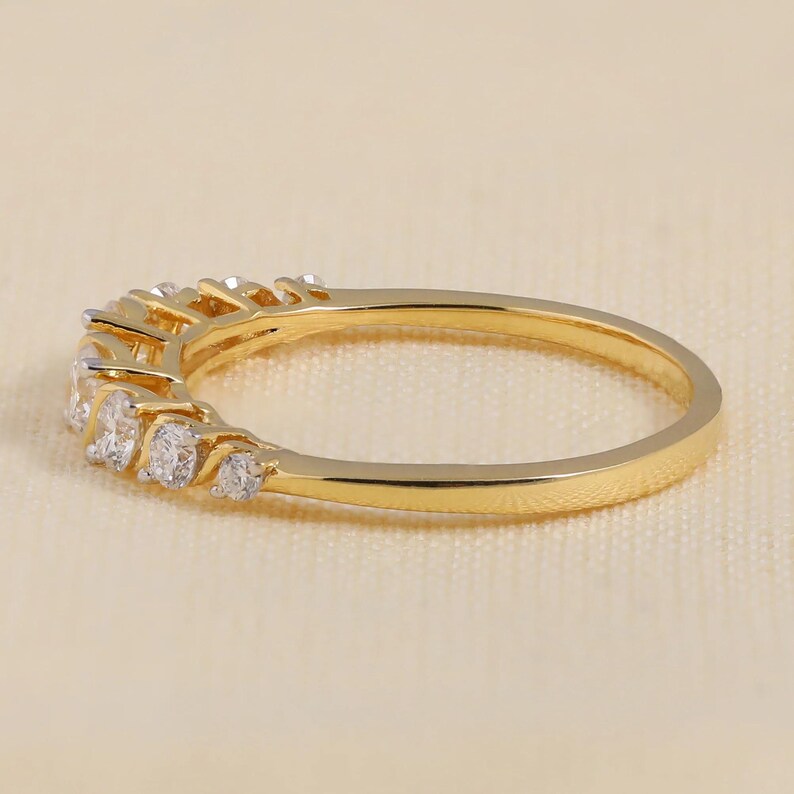 May include: A gold ring featuring a row of small, clear gemstones. The ring has a polished finish and is set against a neutral background. The gemstones are round and evenly spaced. The ring is a classic design.
