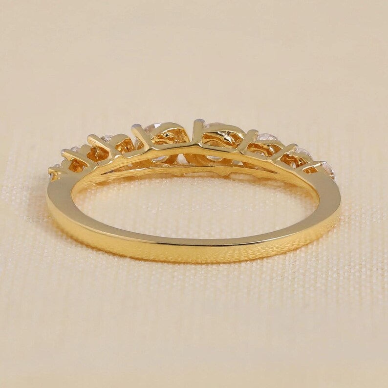 May include: A gold ring featuring a series of clear gemstones. The ring has an ornate design with a polished finish. The gemstones are round and evenly spaced, creating a sparkling effect. The ring is displayed against a neutral background.