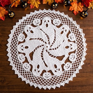 Puede incluir: Un tapete de ganchillo blanco redondo con un patrón repetitivo de fantasmas y pequeñas calabazas de Halloween dispuestos en un diseño circular. El intrincado trabajo de aguja crea un efecto de encaje delicado con un borde festoneado.