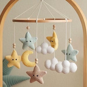 May include: A nursery mobile featuring crocheted stars in yellow, light blue, and beige, a yellow crescent moon, and white clouds, all suspended from a circular wooden frame with small wooden beads on white strings, hanging above a crib.