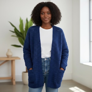 May include: A woman wearing a navy blue, open-front cardigan with two front pockets. The cardigan is made of a chunky knit fabric. She is wearing a white t-shirt and blue jeans.