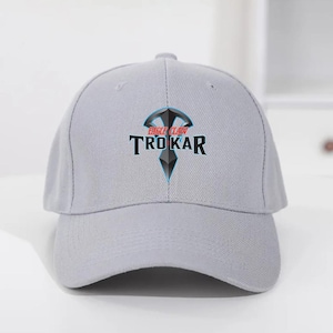 May include: A light gray baseball cap with a curved brim. The cap features the text "TRO KAR" in black, with "EAGLE CLAW" above it, and a geometric design in the center. The hat is made of a durable fabric.