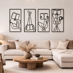 May include: Four black metal wall art pieces showing abstract figures reading books. Each piece is framed in a rectangular black frame. The art is displayed above a beige sectional sofa in a living room setting.