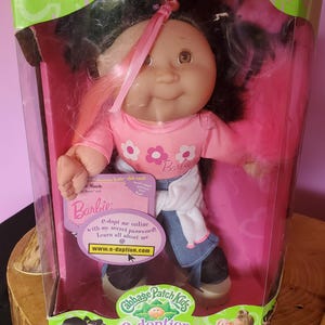 May include: A Cabbage Patch Kids Barbie doll in a clear plastic box. The doll has black hair with pink highlights, a pink shirt with flower graphics, and blue denim pants. The box includes the text "WARNING: CHOKING HAZARD - Small parts. Not for children under 3 years."
