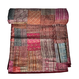 May include: A folded patchwork quilt featuring a mix of patterned fabrics in red, pink, gold, and teal. The quilt displays a variety of textures and designs. A decorative textile, it is made from a selection of fabrics.