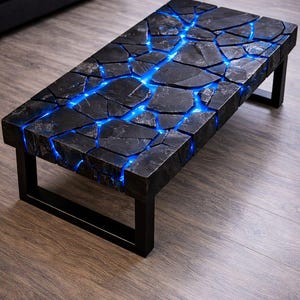 May include: A rectangular coffee table with a black, cracked stone top and a blue glowing resin filling the cracks. The table has a black metal frame and sits on a wooden floor. The table's dimensions are approximately 48 inches long and 24 inches wide.
