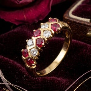 May include: A gold ring featuring an alternating pattern of round red rubies and clear white diamonds set in a honeycomb-style metal structure. The band is polished yellow gold, showcasing a series of five rubies and four diamonds in total.
