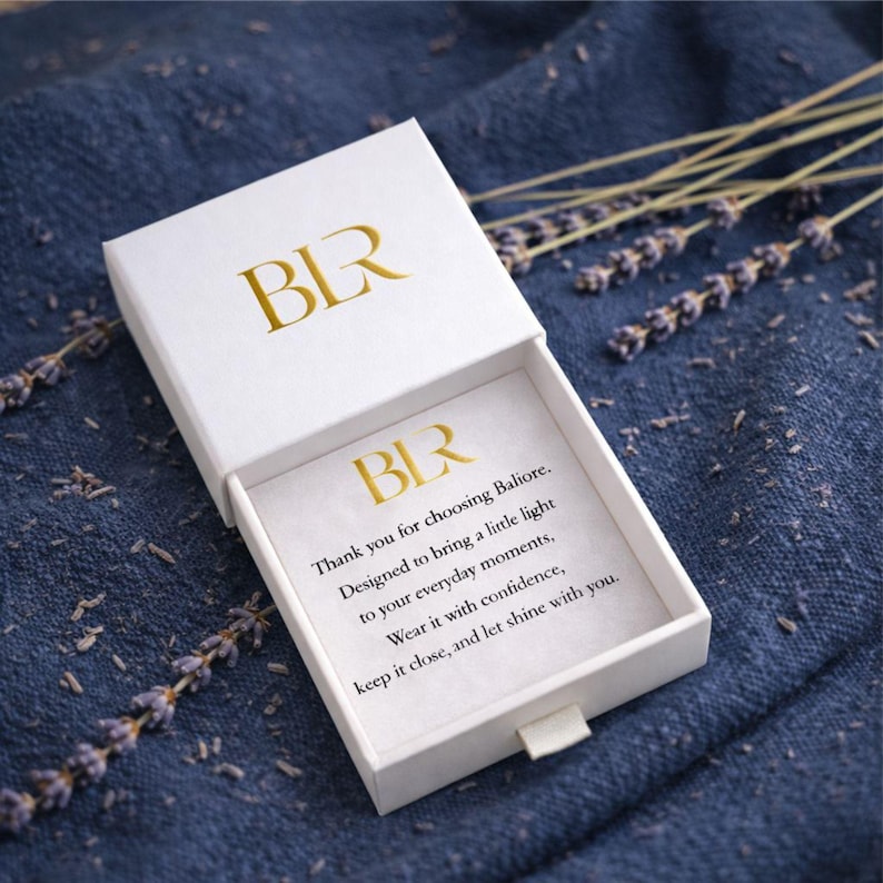 Premium Baliore jewelry gift box with branded thank you card displayed on soft lavender fabric background. Elegant packaging for gold lariat necklace orders, luxury gift presentation, thoughtful women’s jewelry packaging, stylish unboxing experience, ideal for gifting minimalist waterproof necklaces or special occasion jewelry purchases.