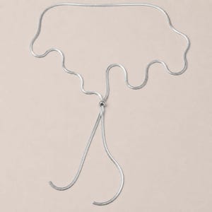 Silver snake chain lariat necklace featuring a polished slider bead and long adjustable chain. Modern bolo tie necklace with minimalist design and versatile styling possibilities. Waterproof jewelry that can be worn as a Y necklace, layering necklace, or long statement necklace. Elegant silver accessory perfect for women who love contemporary jewelry.
