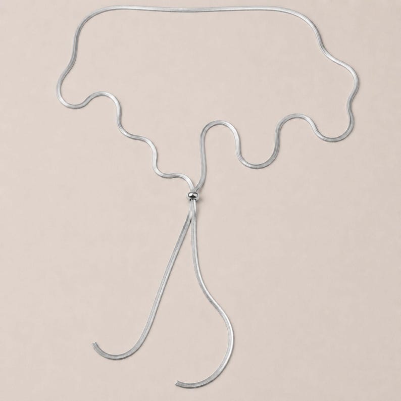 Silver snake chain lariat necklace featuring a polished slider bead and long adjustable chain. Modern bolo tie necklace with minimalist design and versatile styling possibilities. Waterproof jewelry that can be worn as a Y necklace, layering necklace, or long statement necklace. Elegant silver accessory perfect for women who love contemporary jewelry.