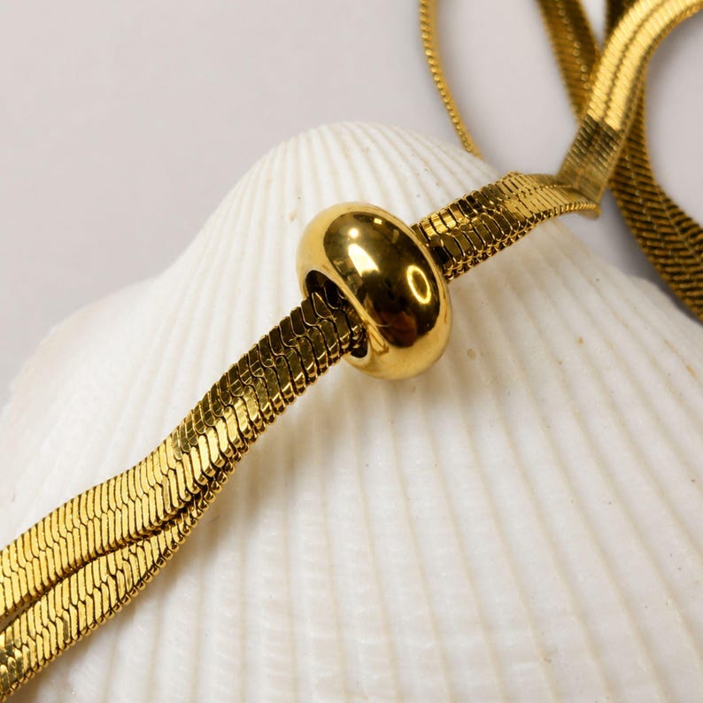 Macro close-up of the polished gold slider bead on a flat snake chain necklace. Detailed product image highlighting the smooth adjustable mechanism and reflective gold finish. Waterproof bolo tie necklace designed for versatile styling, everyday wear, layering, and modern minimalist fashion. Elegant gold jewelry gift for women who love contemporary accessories.