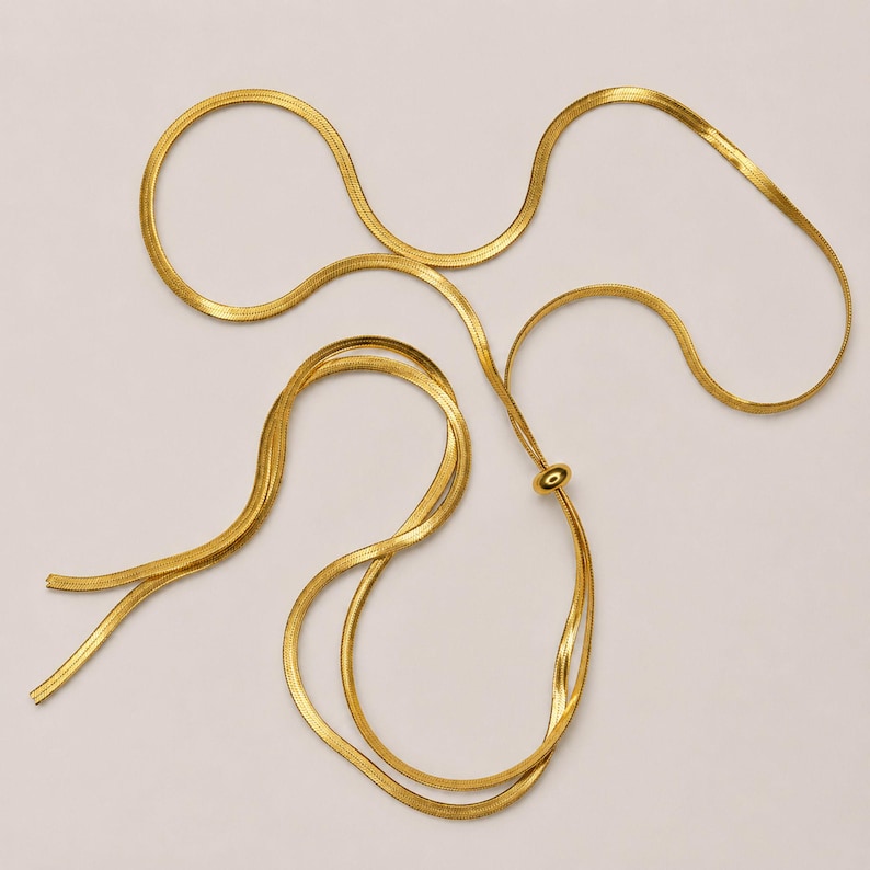 Flat lay display of gold adjustable snake chain bolo necklace arranged elegantly on neutral beige background, showcasing full 120 cm length, polished slider bead, and flexible styling options. Minimalist waterproof jewelry for women, modern lariat necklace, versatile Y necklace, chic statement accessory, sophisticated gift for her.
