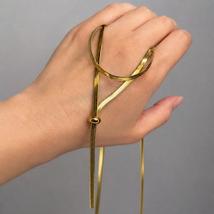 Close-up of gold adjustable bolo tie necklace draped on hand, showcasing flat snake chain texture, polished slider bead, and long lariat drop design. Waterproof gold necklace with minimalist luxury feel, adjustable chain for custom length, modern women’s jewelry piece, sleek Y necklace, perfect gift for her, everyday layering accessory, and elegant statement necklace.