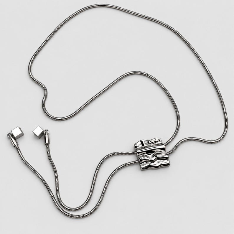 Full product view of a silver tone bolo tie lariat necklace arranged on a clean light background. The long continuous snake chain loops around the sculptural wavy slider and extends into two tassel ends with polished square charms. Clear flat lay shows the adjustable Y necklace construction, statement slider and elegant long necklace proportions for modern everyday styling.