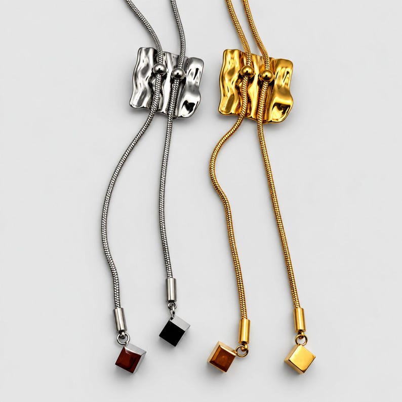 Gold and silver tone bolo tie necklaces shown side by side on a clean light background. Each adjustable lariat necklace features a sculptural wavy slider, flexible snake chain and two long tassel drops finished with geometric square charms. Comparison view highlights both finish options and the distinctive statement Y necklace design, ideal for modern minimalist and everyday styling.