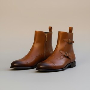 May include: A pair of brown leather ankle boots. One boot features a side zipper with a gold-colored pull, while the other has a buckle closure. The boots have a rounded toe and a low heel, suitable for various occasions.
