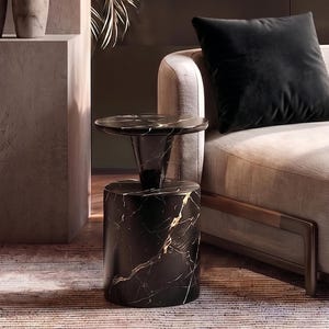 May include: A black marble side table with a cylindrical base and a circular top, positioned next to a low-profile beige upholstered armchair featuring a dark brown frame and a single square black velvet throw pillow resting on the seat.