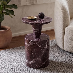 May include: A cylindrical side table crafted from deep purple marble with prominent white veining. The table features a wide circular base, a tapered pedestal support, and a flat circular top. A small gold dish and a dark sphere sit on the surface.