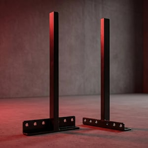 May include: Two black metal T-shaped shelf brackets with vertical posts and horizontal bases featuring pre-drilled circular mounting holes. The brackets have a matte finish and a sturdy, industrial design intended for wall-mounted shelving support.