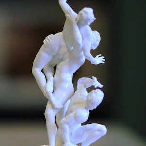 May include: A white sculpture of three figures in motion. One kneels, another supports a third figure reaching upwards. The sculpture is on a rectangular base and has a smooth finish. The figures are in a dynamic pose.