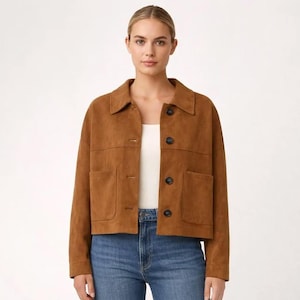 May include: A brown suede jacket with a collared neckline, two front pockets, and black buttons. The jacket is worn over a white top and paired with blue jeans. A classic outerwear piece.