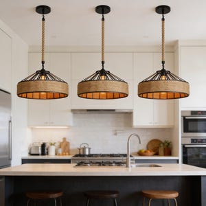 Könnte beinhalten: Drei Pendelleuchten im rustikalen Design hängen über einer Kücheninsel. Jede Leuchte hat einen schwarzen Metallrahmen, einen gewebten beigefarbenen Schirm und ein Naturseil. Die Leuchten sind an schwarzen Deckenhalterungen aufgehängt.