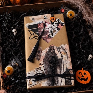 Könnte beinhalten: Eine rechteckige Geschenkbox in braunem Papier mit einer Sensenmann-Illustration, einer schwarzen Quaste und einer schwarzen Schleife. Die Box enthält verschiedene Halloween-Aufkleber, darunter Totenköpfe und eine Hexe, eingebettet in schwarzes Papier.