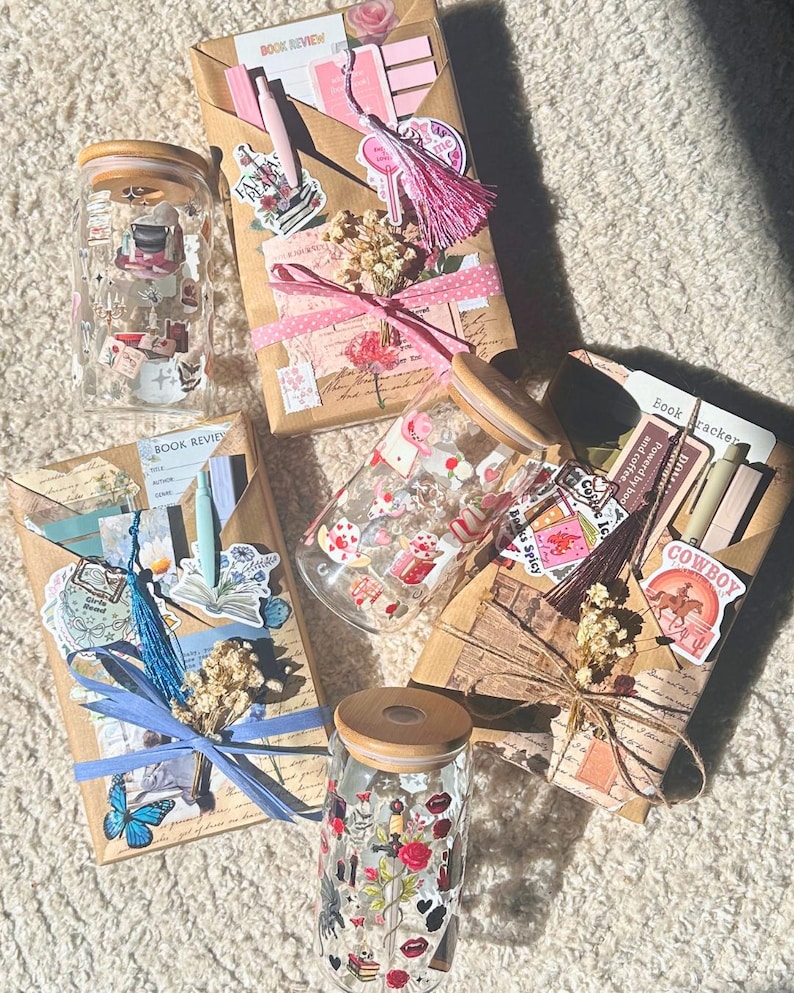 Könnte beinhalten: Eine Auswahl an dekorativen Glasbehältern mit Holzdeckeln und verpackten Paketen. Die Gläser sind mit Aufklebern und Illustrationen verziert. Die Pakete sind in braunes Papier gewickelt und mit Bändern, Aufklebern und Trockenblumen verziert. Einige Pakete tragen den Text "BOOK REVIEW".